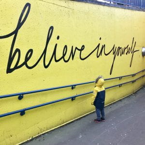 A small child looking at a wall that says believe in yourself