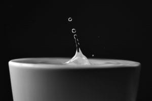 A droplet of water suspended above a full cup