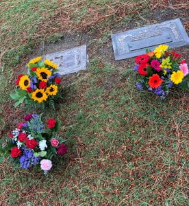 Photo of three bunches of flowers in front of two gravestones