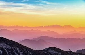 A picture of mountains with a sky layered in colors: purple, orange, yellow and blue