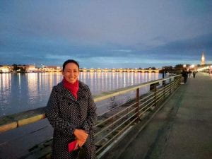 An Asian American woman standing in front of the Garonne river with the Pont de Pierre behind her
