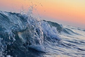 photograph of a wave breaking with a backdrop of sunset