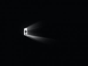 A black room with a small frame of light and an individual standing in the door