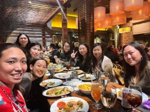 Photograph of a table with Thai food and 8 Asian American women around it