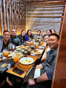 Photograph of a long table with Thai food on it and Asian American people around it