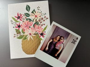 Photo of a card with a vase of flowers and a polaroid picture of two Asian American women standing in front of a door