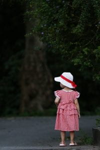 Photograph of a little girl in a red dress with a white hat with red ribbon