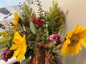 Photograph of a bouquet of flowers including yellow sunflowers, pink/lavender roses and assorted wildflowers