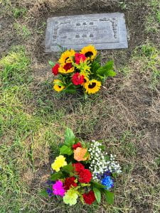 Picture of a grave stone with two bouquets of flowers in front of them