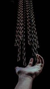hand with multiple chains floating above it on a black background