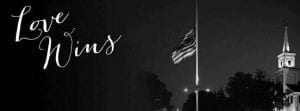 Black and white photo of a flag lowered to half mast with a church tower in the background and the words Love Wins in script on the left side