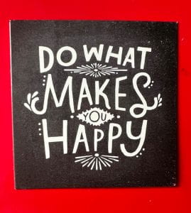 Photo of a small square black card on a red background with "Do what Makes you Happy" written in white script