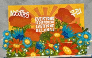 Photograph of a mural with bright orange and blue flowers that reads Everyone is Different, Everyone Belongs