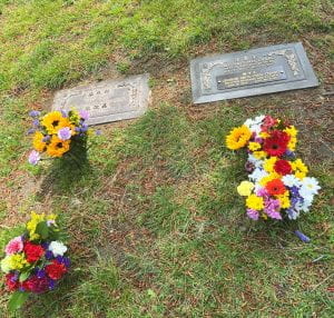 Photograph of two grave markers with 4 bouquets of flowers in front of them