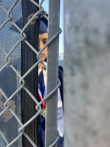 Photo of a person (my son) in a graduation cap and gown as taken through a fence